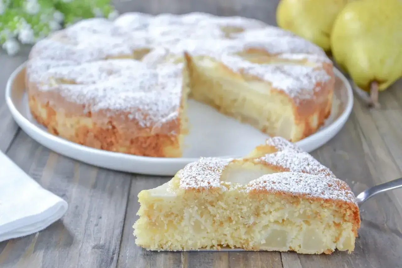 Una fetta di torta pere soffice e profumata, cosparsa di zucchero a velo, su un tavolo di legno.