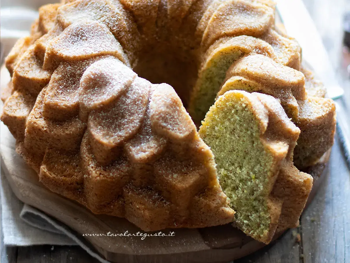 Una deliziosa torta al pistacchio, soffice e profumata, cosparsa di zucchero a velo. La fetta rivela il suo colore verde brillante.