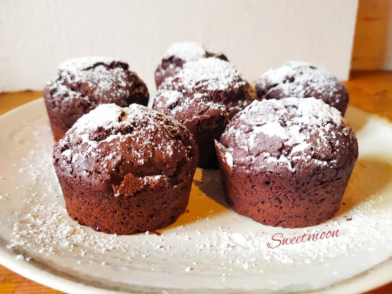 Cinque muffin al cioccolato senza burro, spolverati di zucchero a velo, su un piatto chiaro.