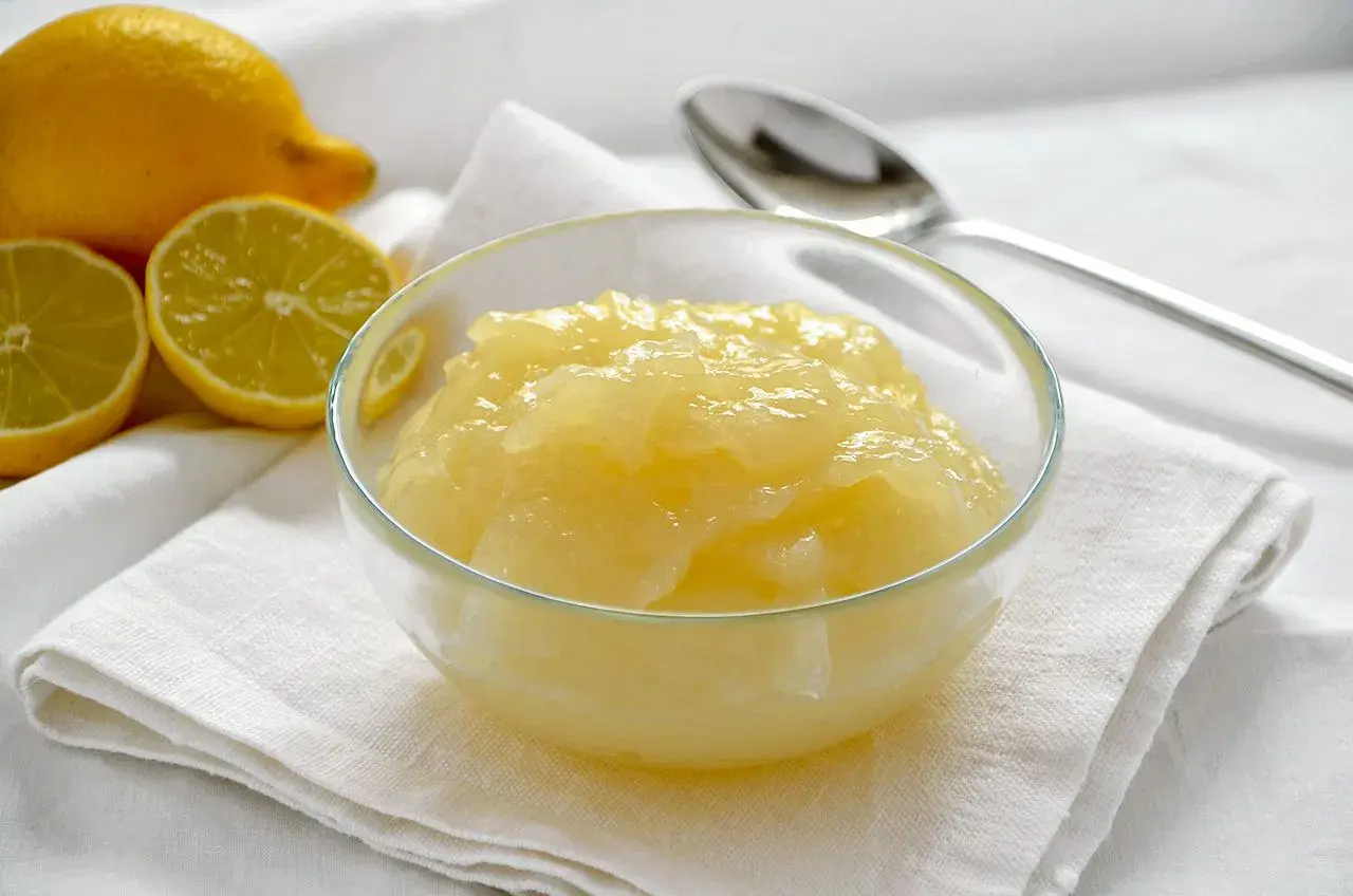 Una ciotola di cremosa crema al limone, con limoni freschi affettati sullo sfondo.