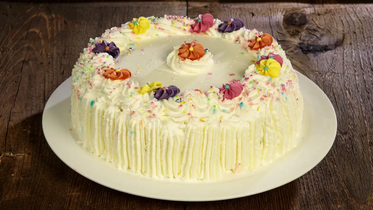 Torta compleanno uomo con panna, decorata con fiori colorati e codette, pronta per festeggiare.