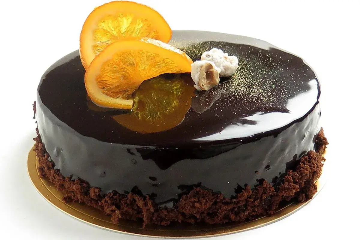 Torta lucida al cioccolato con fette d'arancia candita e nocciole. Un delizioso mousse cioccolato e arancia che invita a un assaggio.
