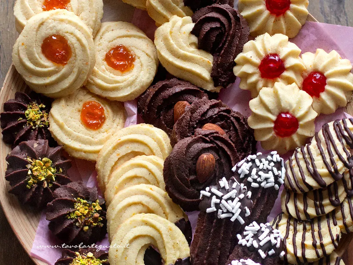 Variazioni di frolla montata: biscotti al cacao con mandorle e pistacchi, frollini con marmellata d'arancia e ciliegia, e decorati con cioccolato.