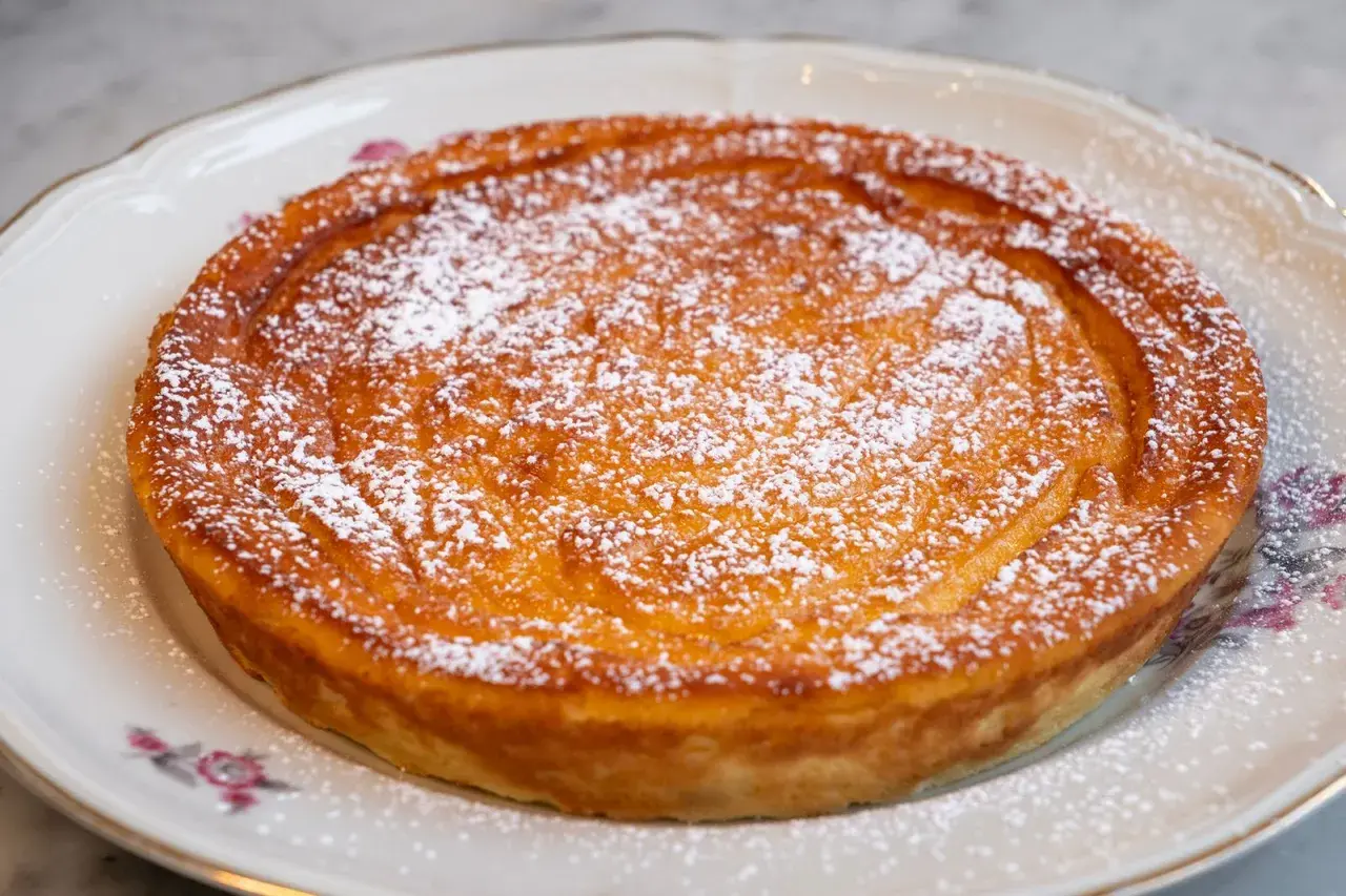 Migliaccio napoletano ricetta della nonna, dorato e cosparso di zucchero a velo, su un piatto decorato.