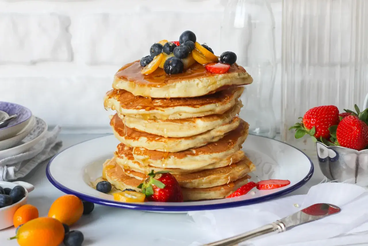 Pancake perfetti, dorati e soffici, pronti per essere gustati. Ecco come fare i pancake per una colazione da campioni, guarniti con frutti di bosco e sciroppo.