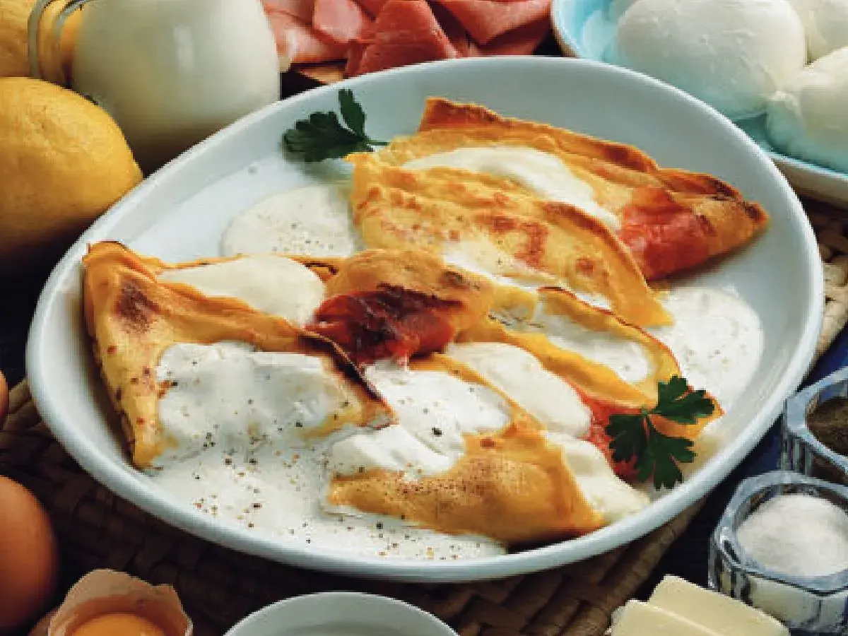 Crepes ripiene di prosciutto e formaggio, condite con una salsa cremosa. Una deliziosa panna acida ricetta per un piatto unico.