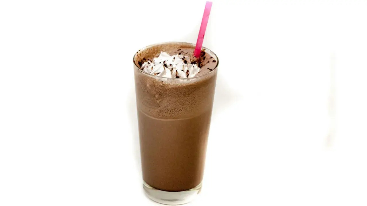 Un delizioso frappè al cioccolato, guarnito con panna montata e scaglie di cioccolato, pronto per essere gustato con una cannuccia rosa.
