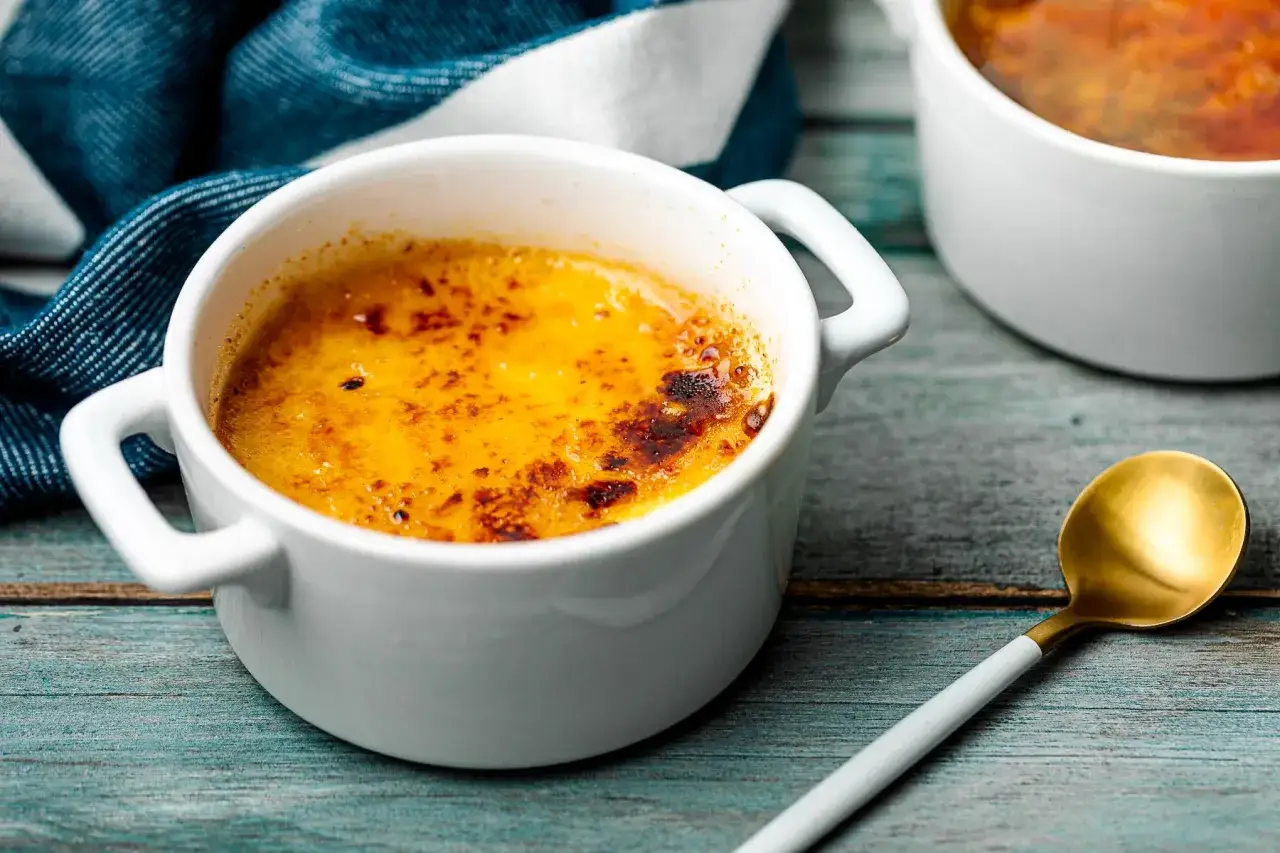 Delizioso creme brulee con croccante caramello dorato, pronto per essere gustato con un cucchiaino dorato.