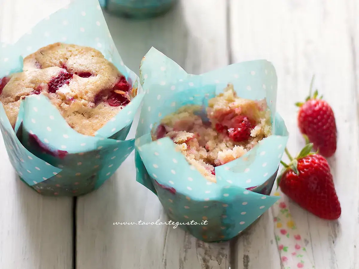 Due muffin alle fragole in pirottini azzurri a pois bianchi, con fragole fresche accanto.