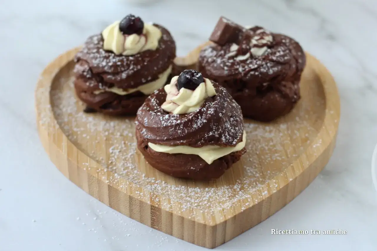 Tre deliziose zeppole al cacao, ripiene di crema e decorate con ciliegie e zucchero a velo, su un vassoio a forma di cuore.