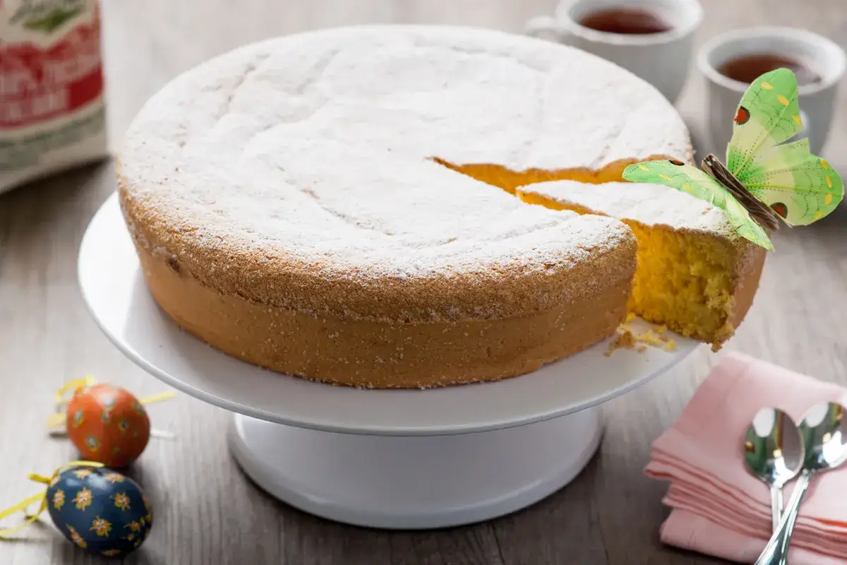 Torta nuvola soffice e leggera, cosparsa di zucchero a velo, con una fetta tagliata e una farfalla verde posata sopra.