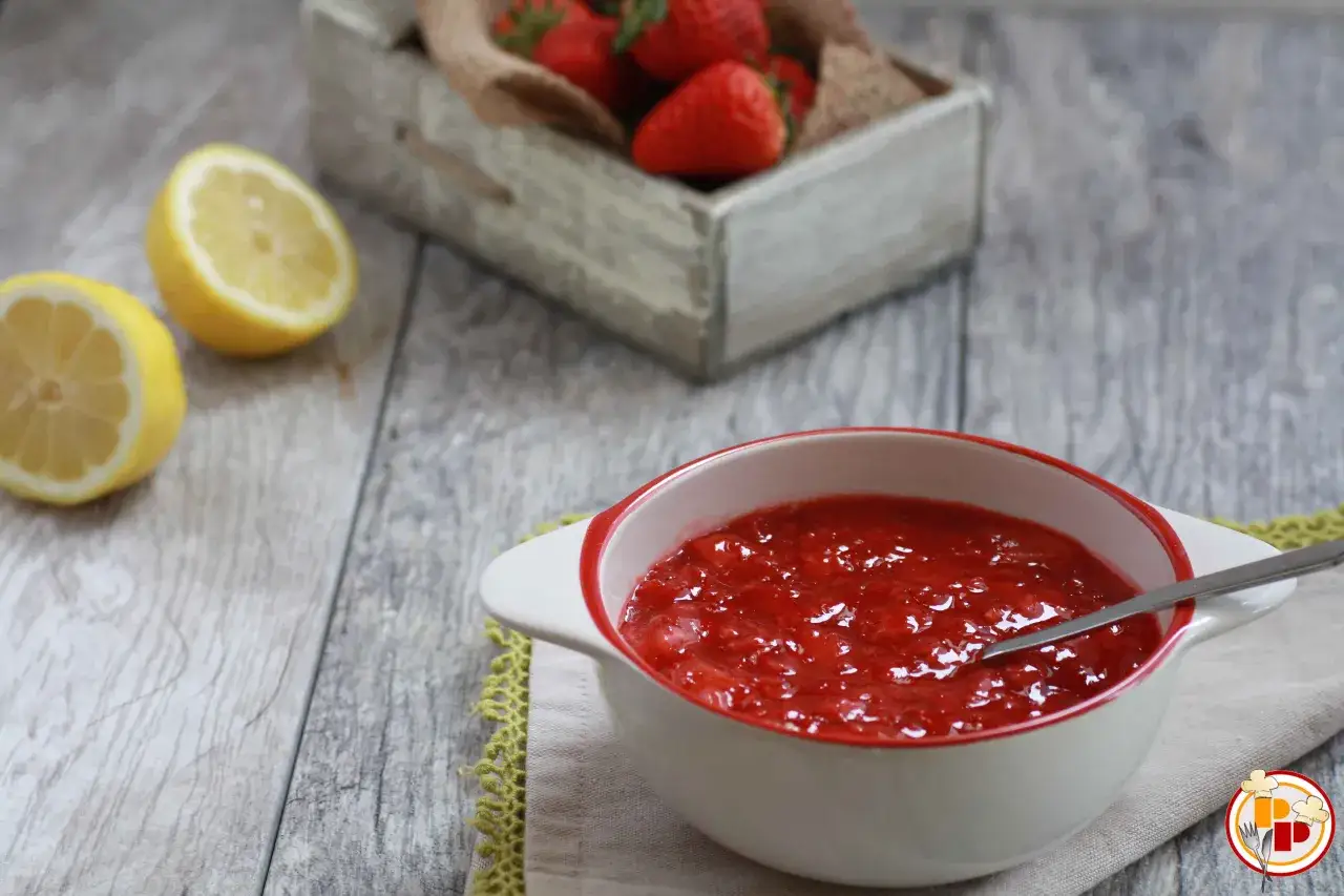 Una ciotola di coulis di fragole, con limoni e fragole fresche sullo sfondo.