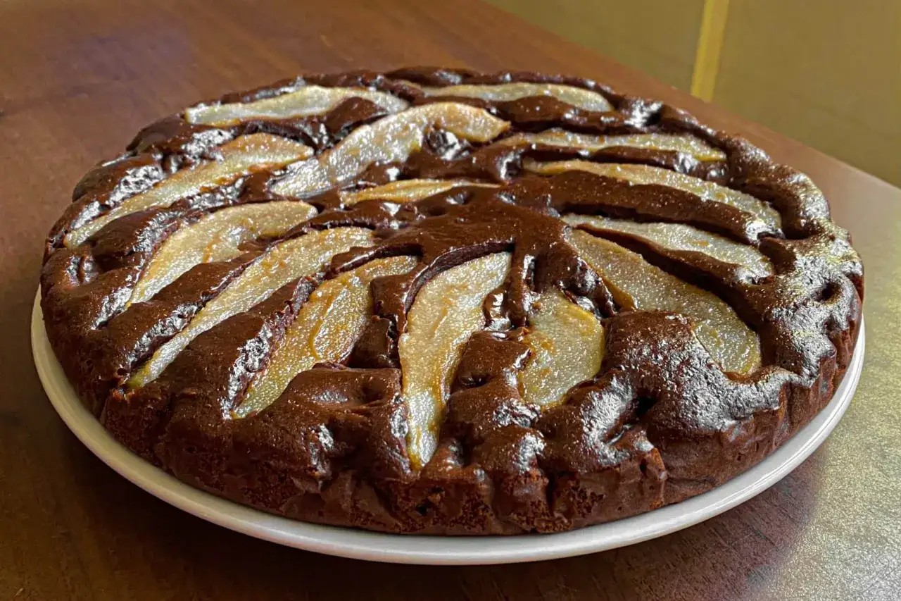 Torta pere e cioccolato, con fette di pera disposte a raggiera su una base scura e umida, pronta per essere gustata.