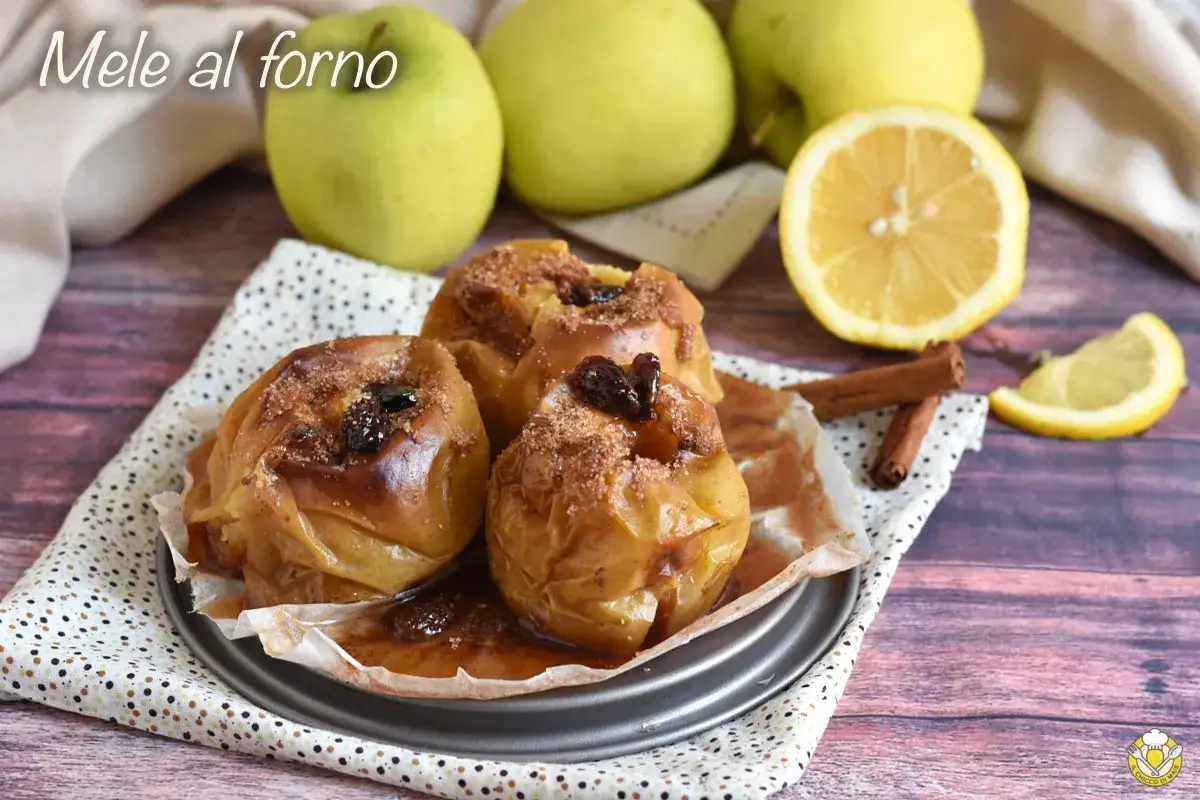 Mele cotte al forno, dorate e profumate, con uvetta e cannella. Accanto, mele fresche, limone e bastoncini di cannella.