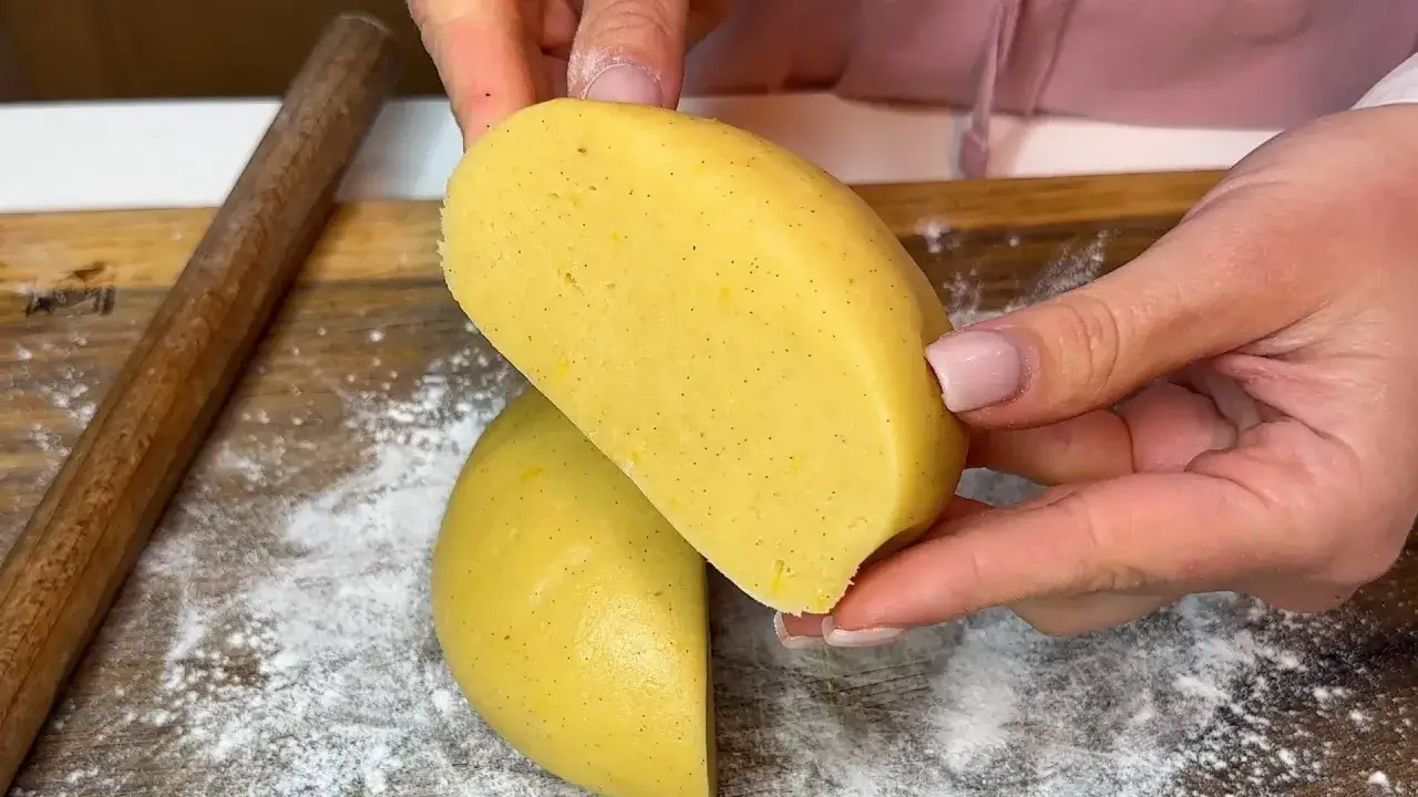 Mani che tengono un impasto giallo chiaro, con puntini scuri di vaniglia. &Egrave; la pasta frolla senza burro, pronta per essere lavorata.