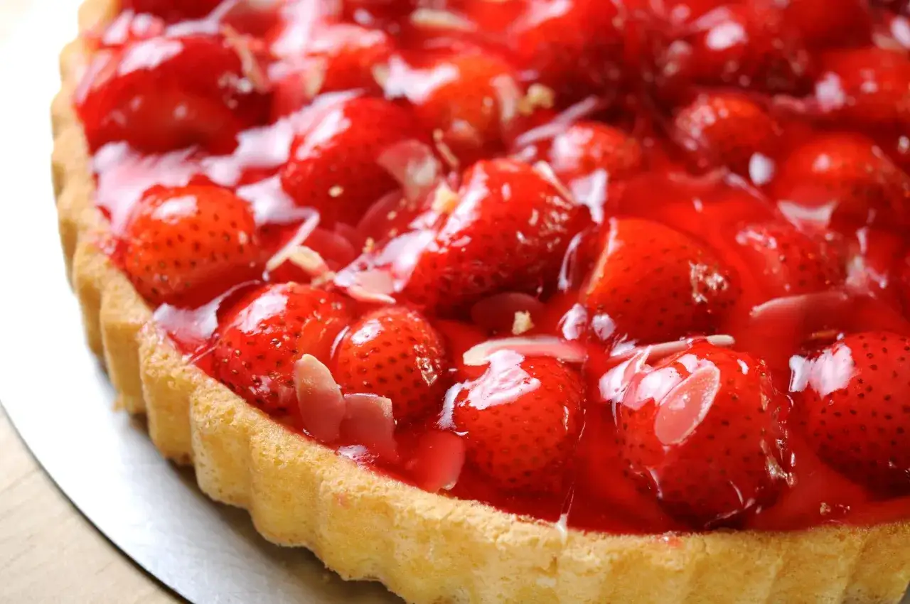 Torta di fragole lucida e invitante, con fragole fresche intere e a fette ricoperte da una gelatina rossa brillante e scaglie di mandorle.