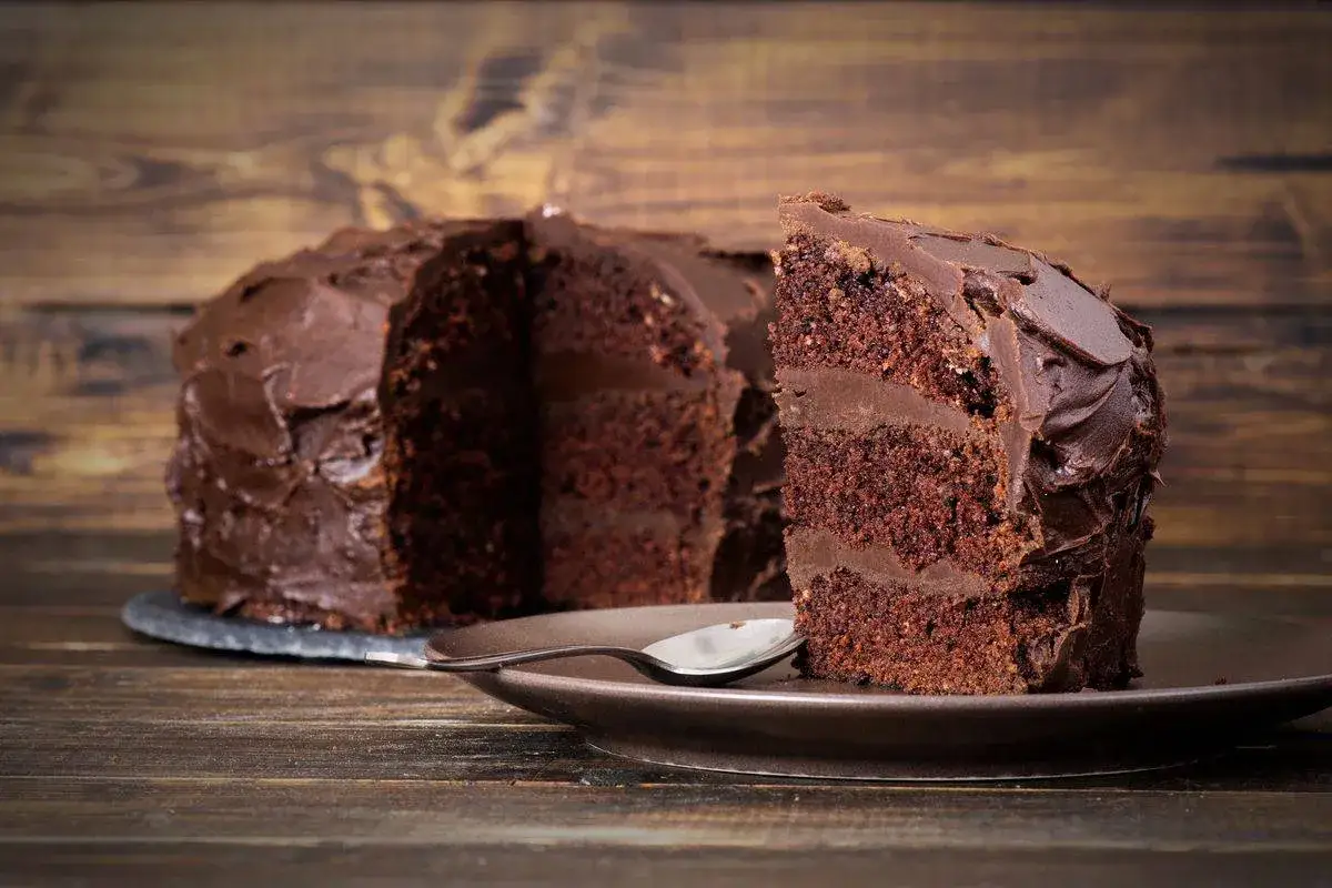 Una fetta di torta al cioccolato, un vero mud cake, su un piatto marrone con un cucchiaino.