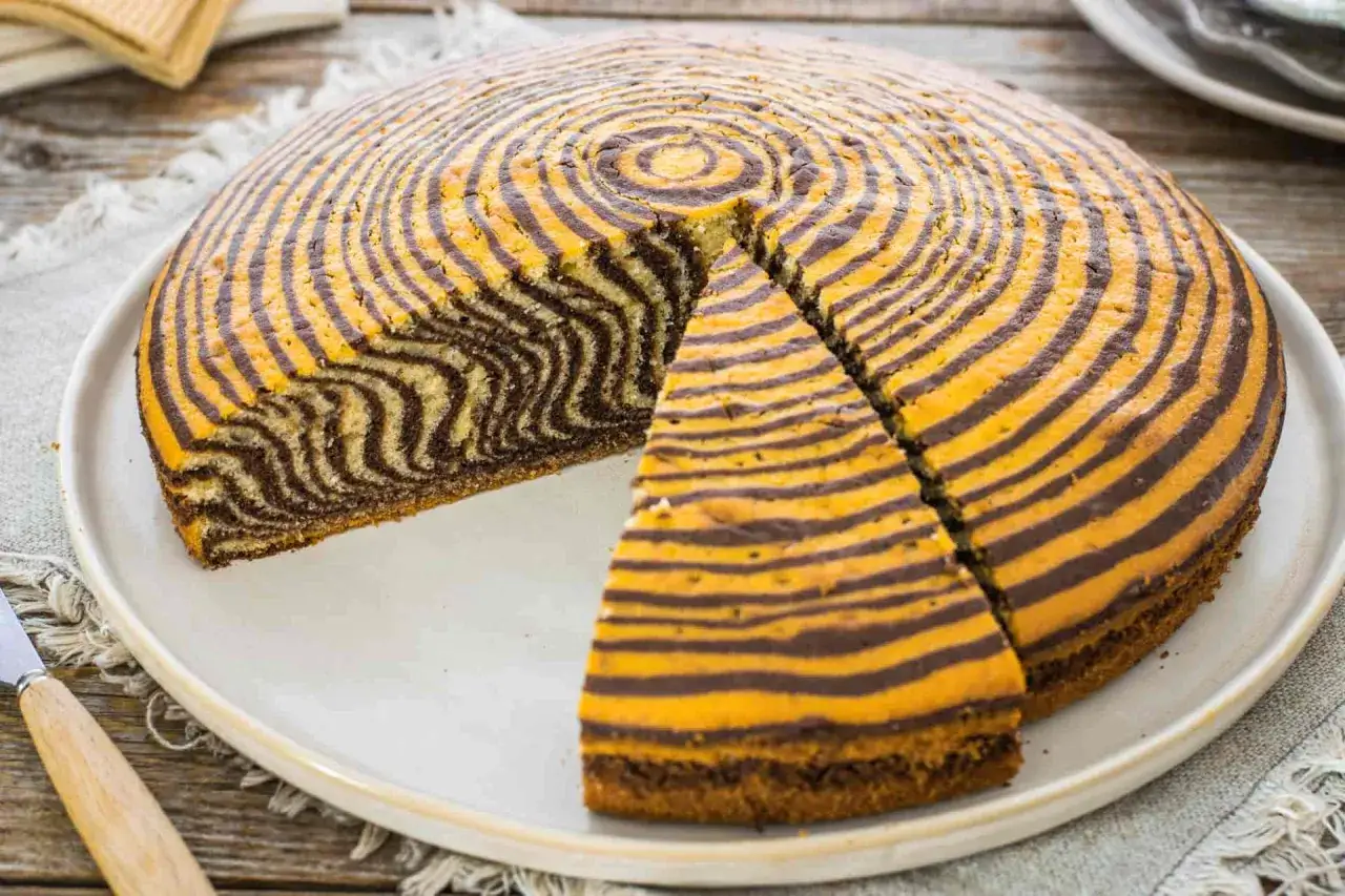 Torta zebrata con un motivo a spirale di strisce marroni e gialle, una fetta è stata tagliata.