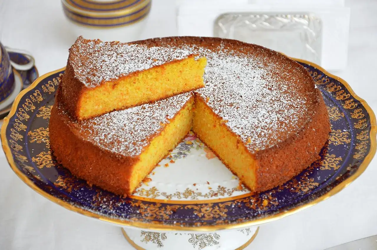 Una deliziosa torta carote e mandorle, cosparsa di zucchero a velo, servita su un elegante piatto decorato.