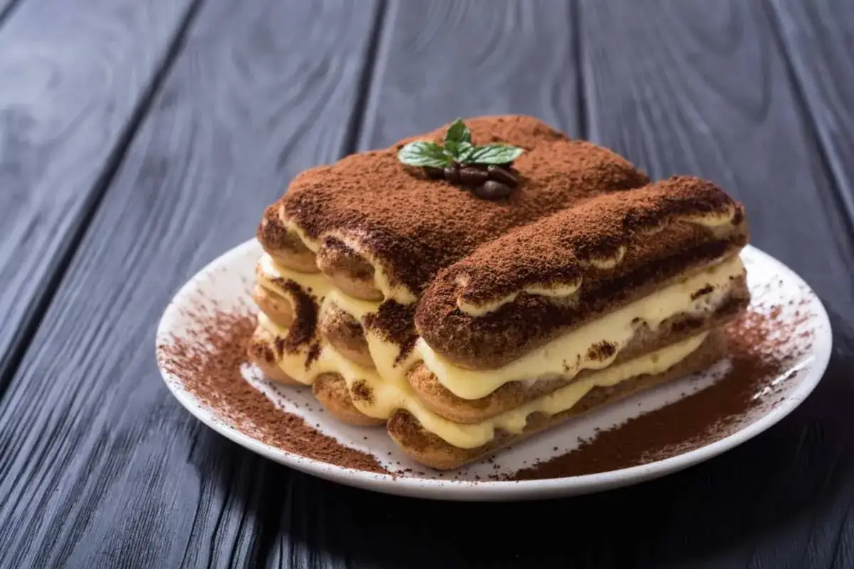 Delizioso tiramisù con crema pasticcera, ricoperto di cacao e decorato con menta e chicchi di caffè.