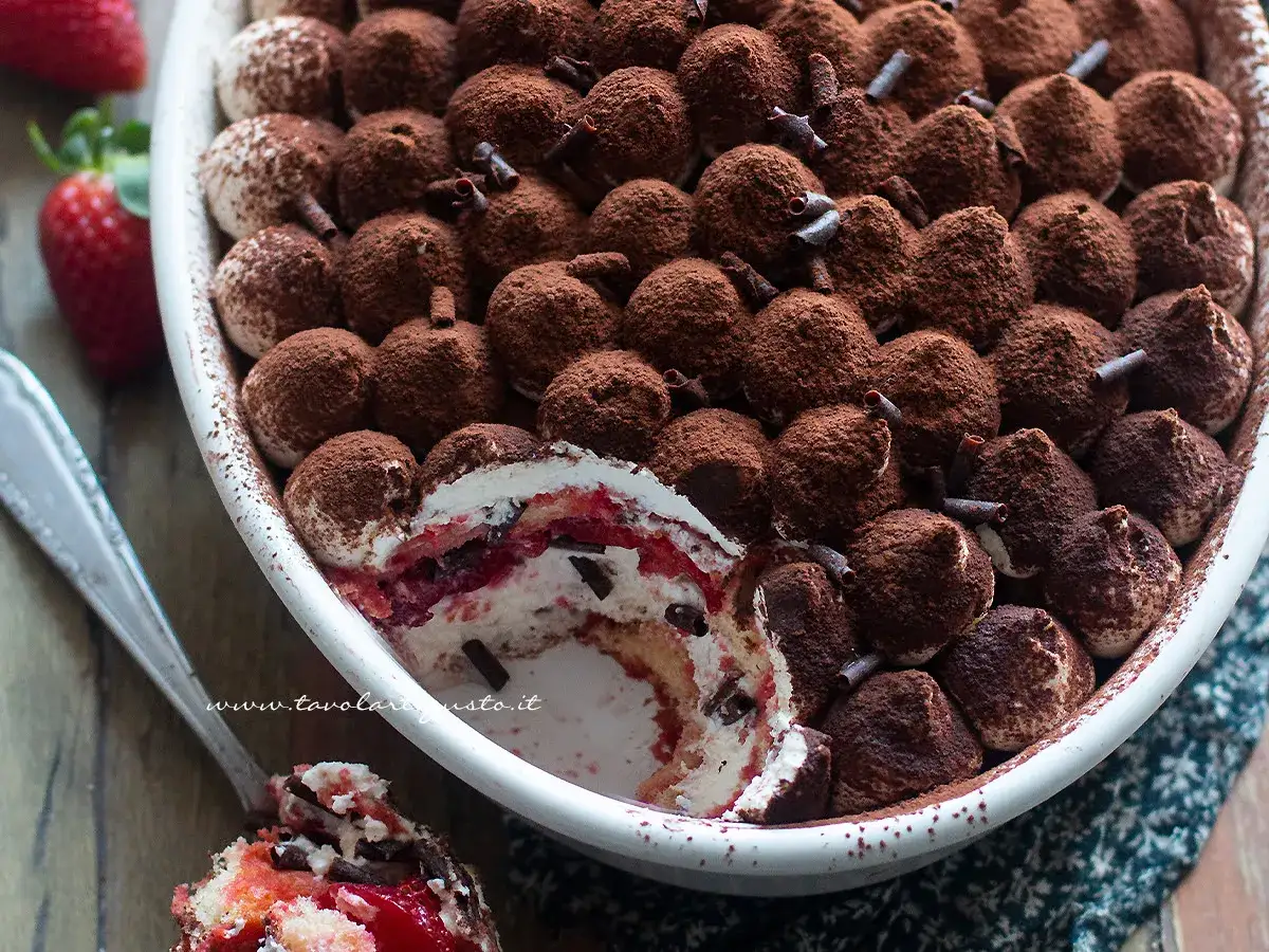Delizioso tiramisù con fragole e cioccolato, cosparso di cacao amaro e decorato con riccioli di cioccolato.
