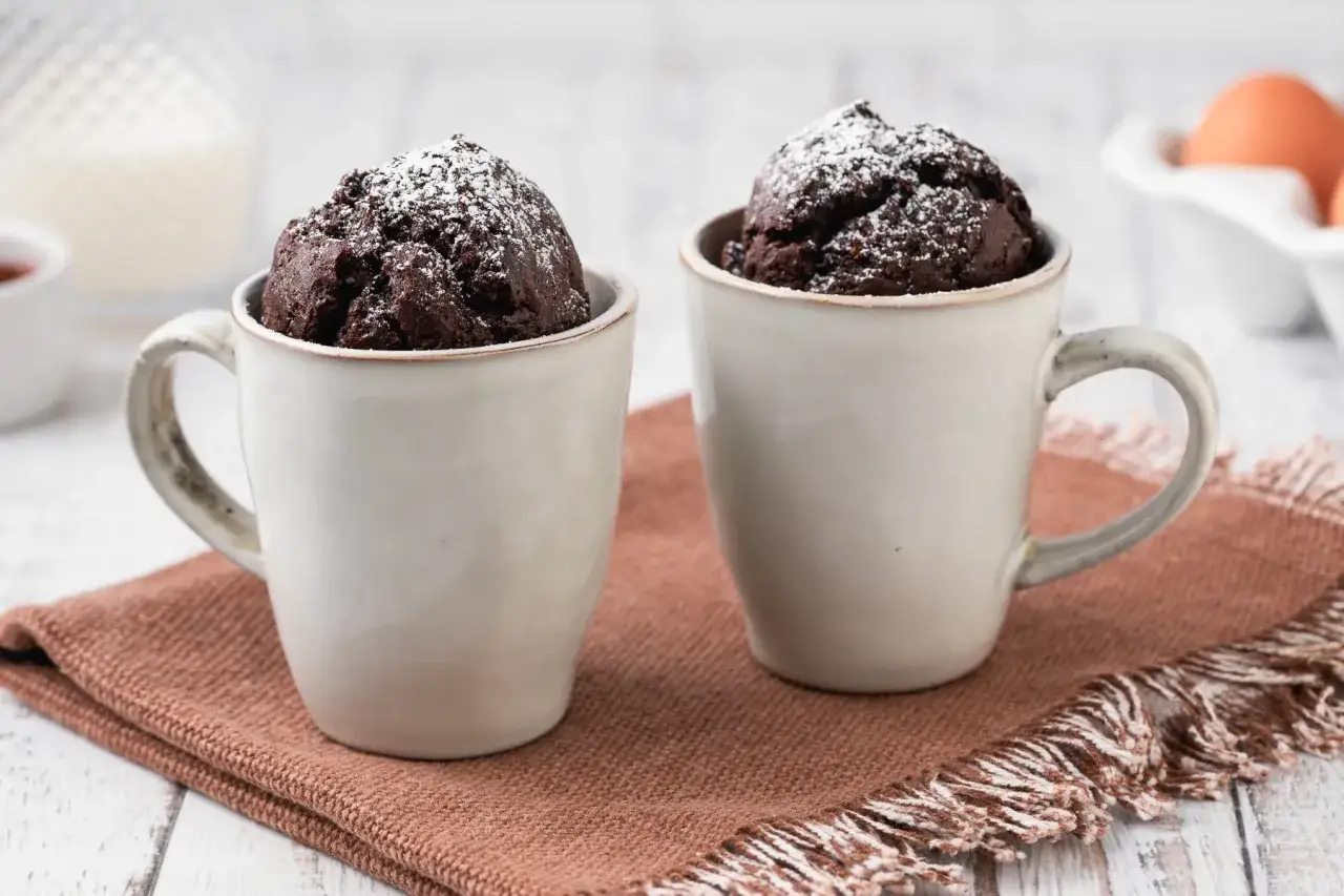 Due mug cake al cioccolato, spolverate di zucchero a velo, pronte per essere gustate.