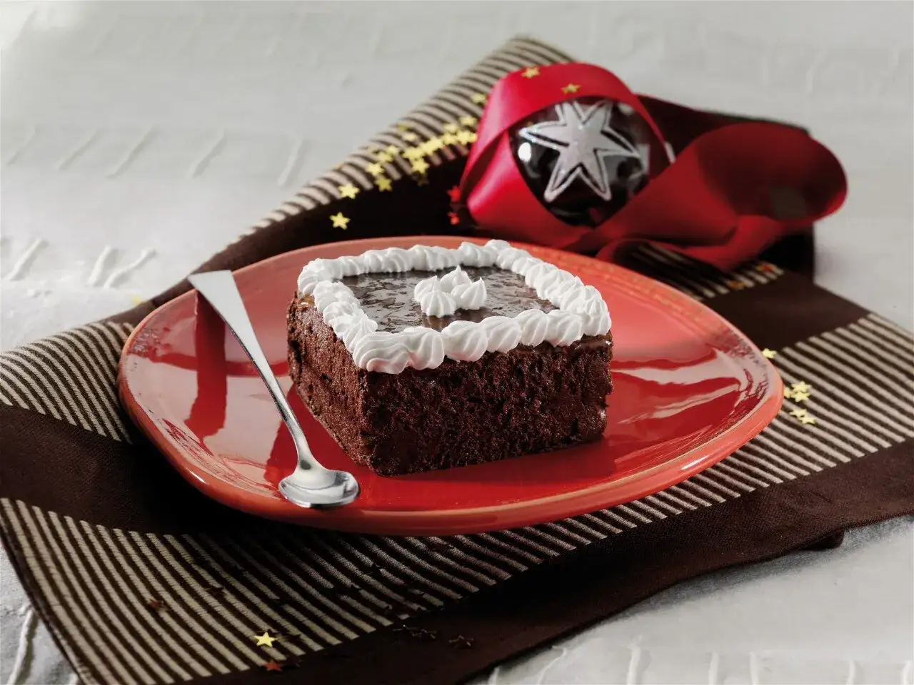Una deliziosa mattonella di cioccolato, decorata con panna montata, su un piatto rosso, pronta per essere gustata.