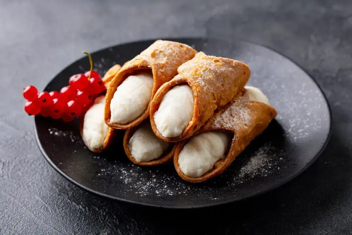 Cannoli siciliani con la loro cremosa farcitura, guarniti da ribes rossi e zucchero a velo.