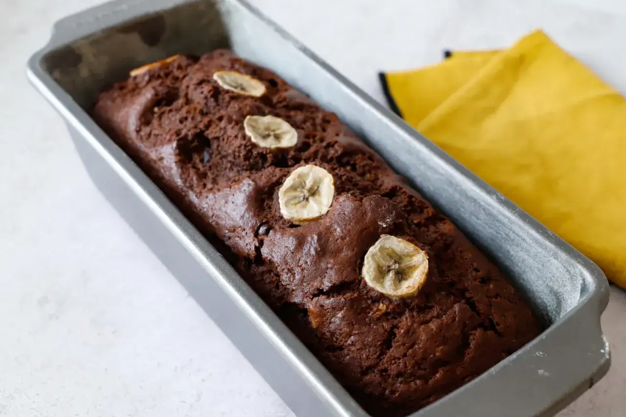 Dolce banana e cioccolato appena sfornato in uno stampo, decorato con fette di banana.