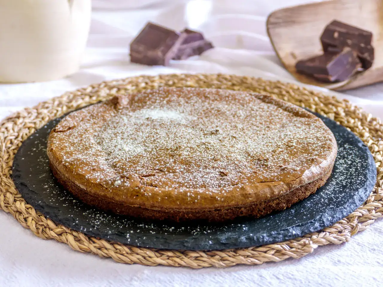 Torta tenerina Bimby, soffice e golosa, cosparsa di zucchero a velo. Pezzi di cioccolato fondente sullo sfondo.