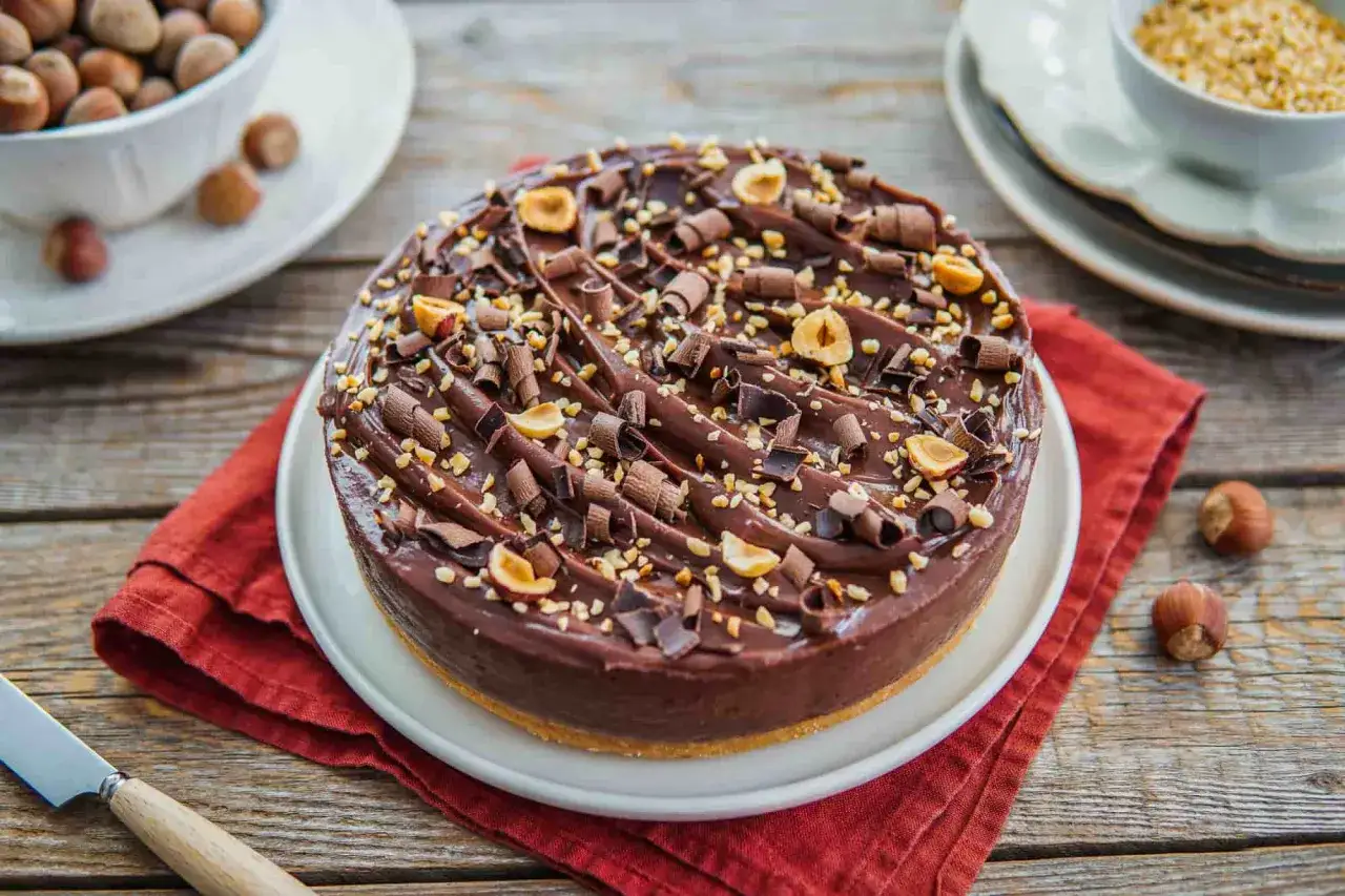 Cheesecake alla Nutella e mascarpone, decorata con riccioli di cioccolato e nocciole tostate.