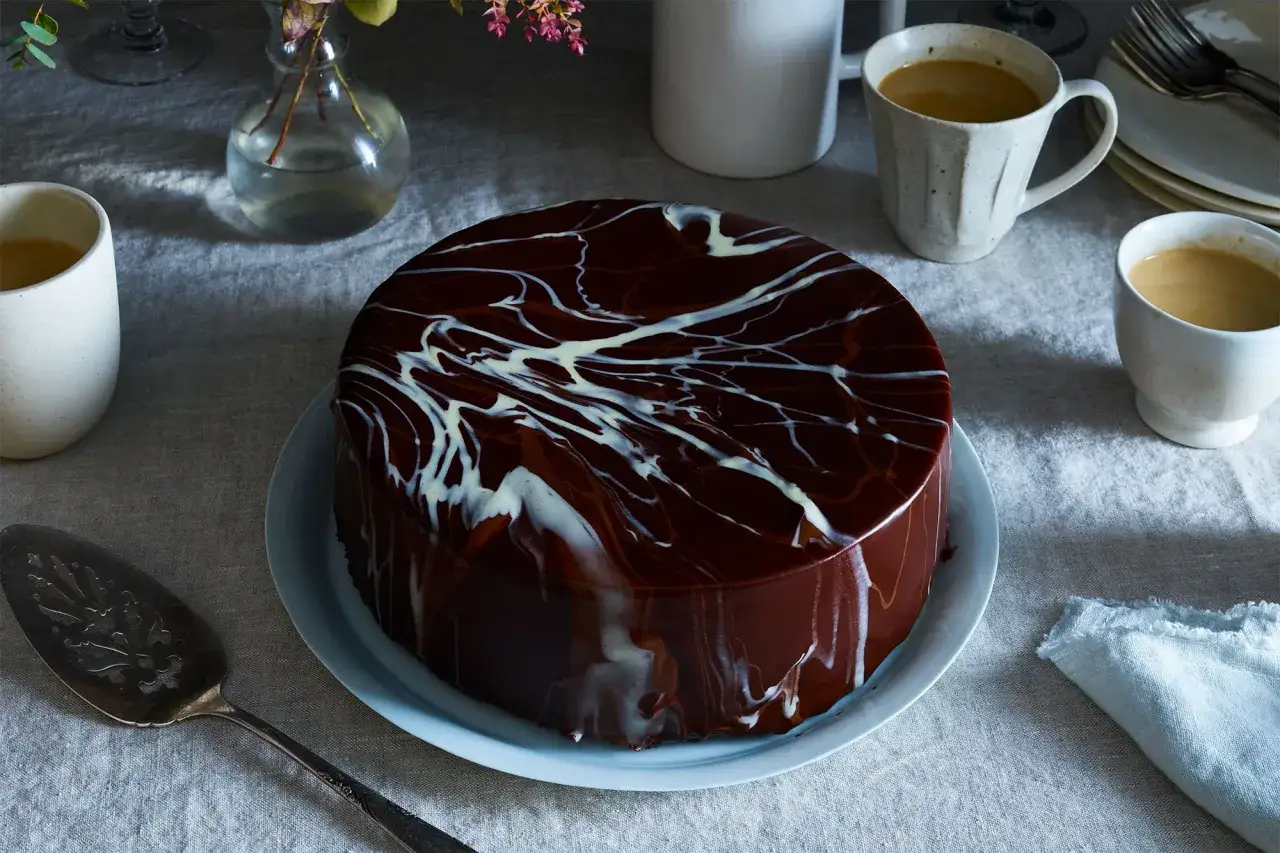 Torta lucida con glassa al cioccolato e decorazioni bianche, pronta per essere servita con caff&egrave;.