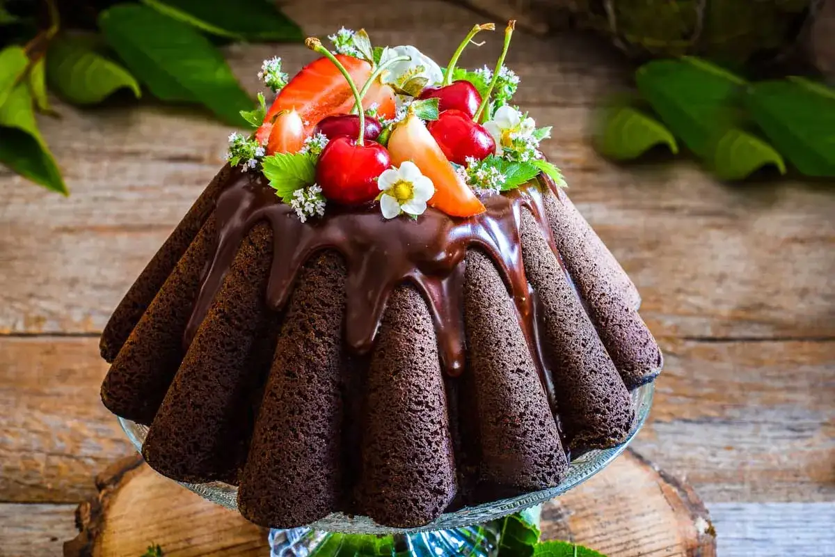 Delizioso bundt cake ricetta al cioccolato, decorato con fragole, ciliegie e fiori freschi.