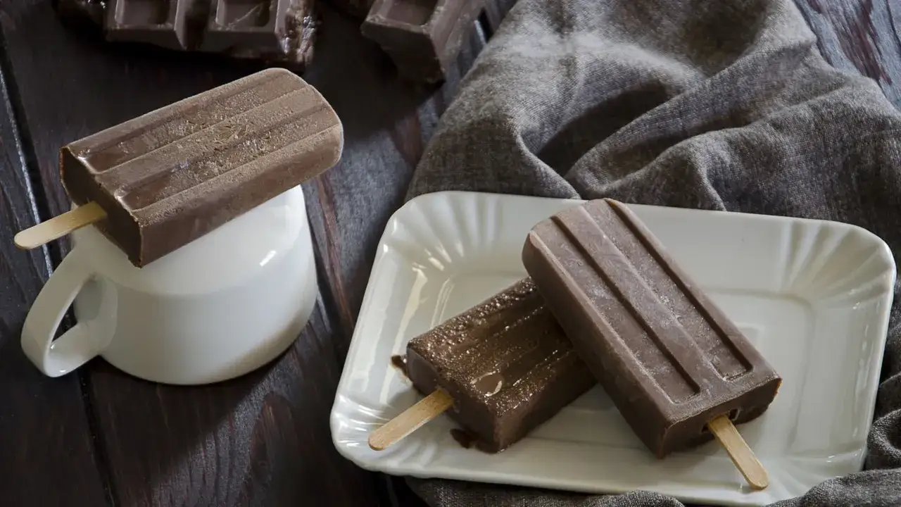 Tre ghiaccioli al cioccolato, uno su una tazza bianca, gli altri su un piatto, con pezzi di cioccolato sullo sfondo.