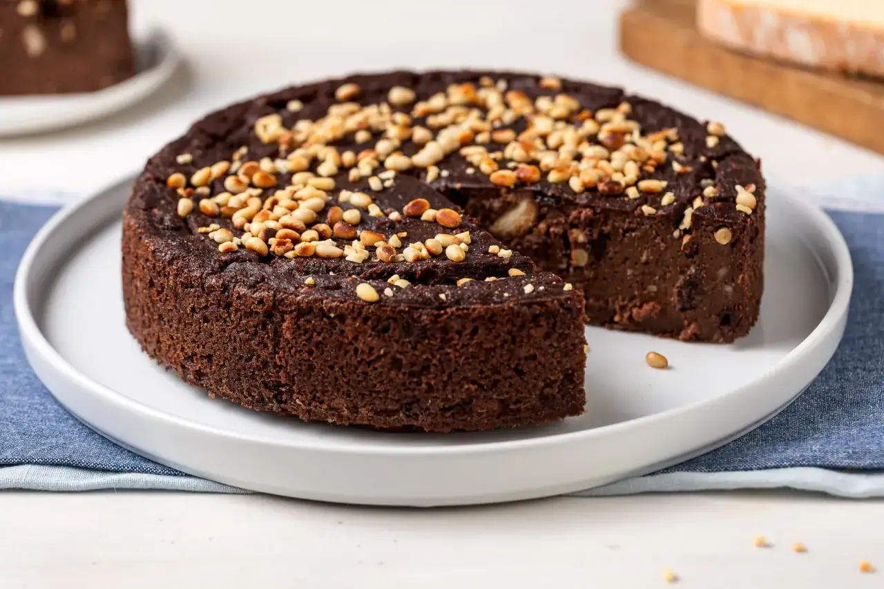 Torta al cacao zuccherato, ricca e umida, guarnita con pinoli tostati. Un dolce irresistibile per ogni occasione.