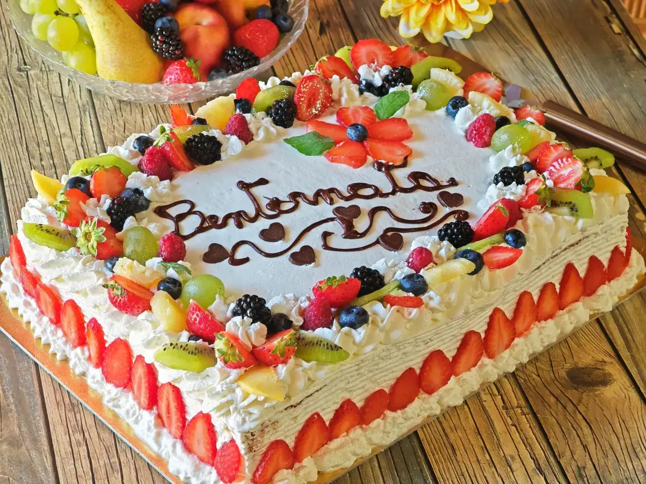 Torta compleanno decorata con panna, fragole, kiwi, mirtilli e lamponi. Scritta