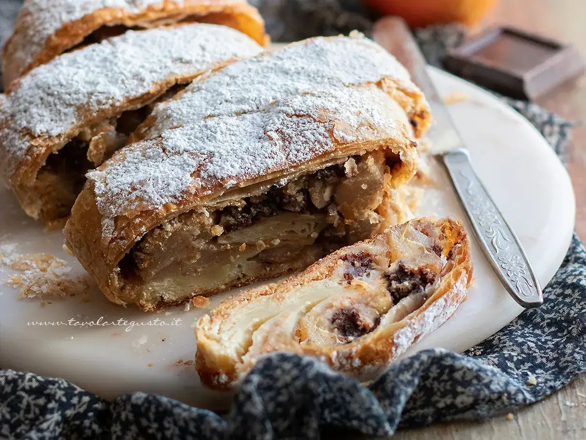 Delizioso strudel al cioccolato cosparso di zucchero a velo, con un morso invitante che rivela il ripieno goloso.