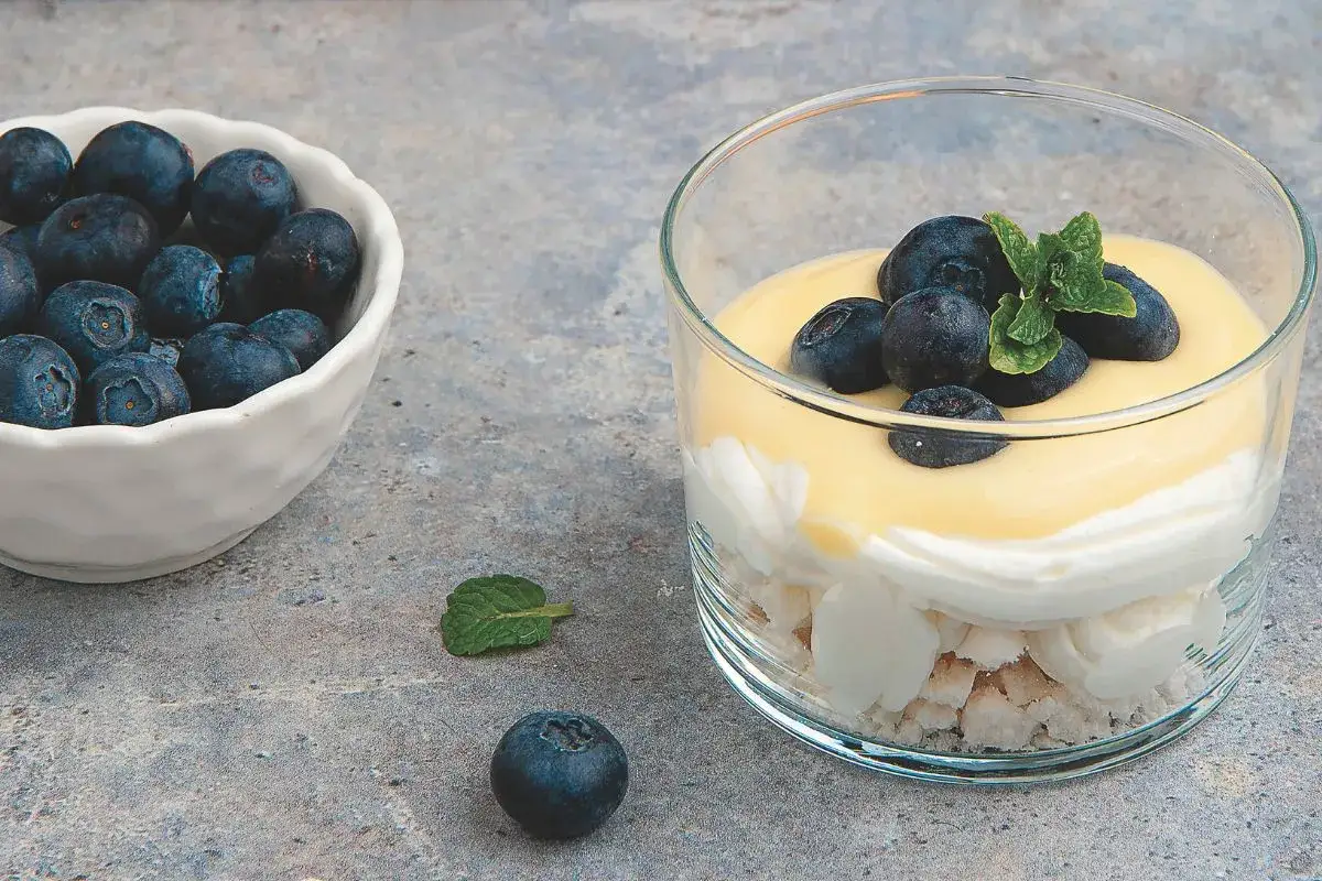 Deliziosi dolci al cucchiaio con meringa, panna, crema pasticcera e mirtilli freschi, guarniti con menta.