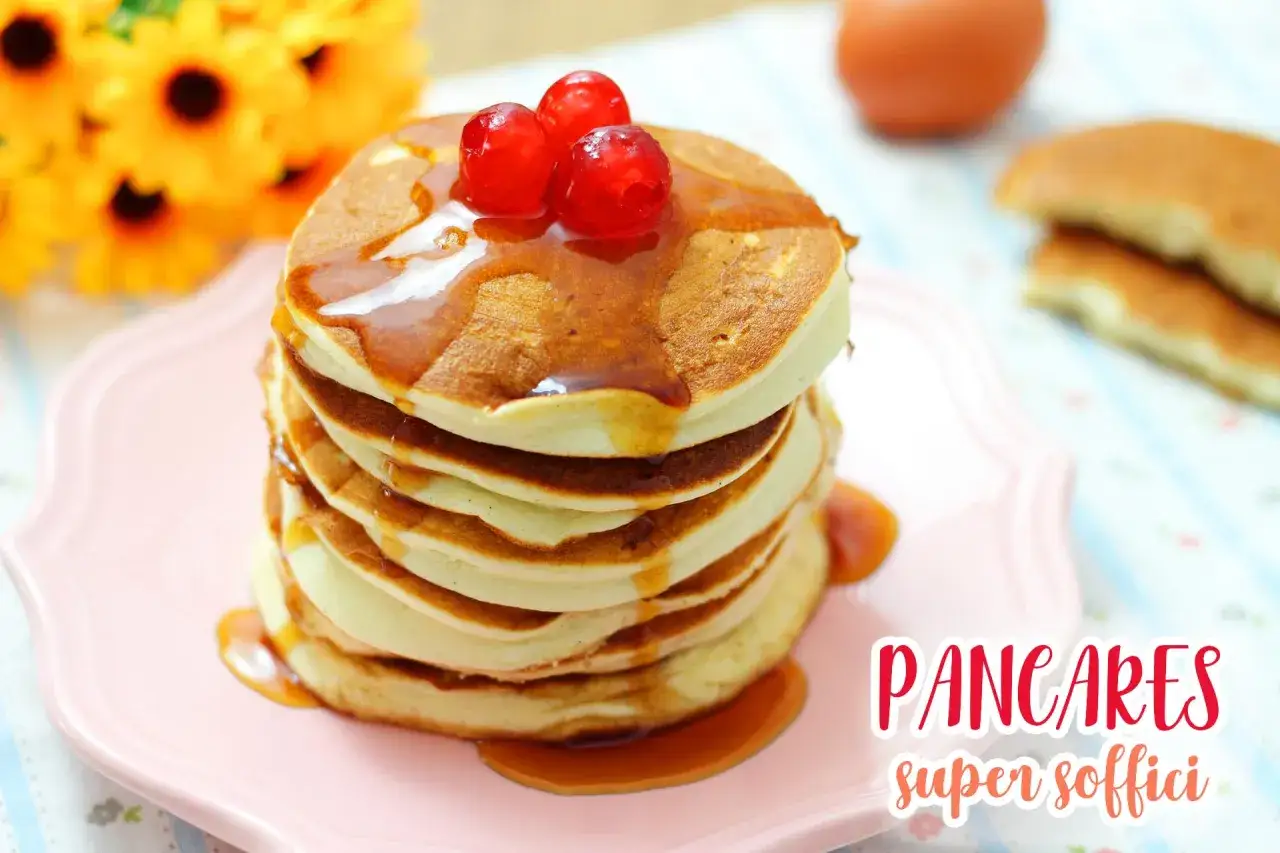 Pancakes super soffici, una pila dorata con sciroppo e ciliegie rosse, pronti per una colazione leggera.