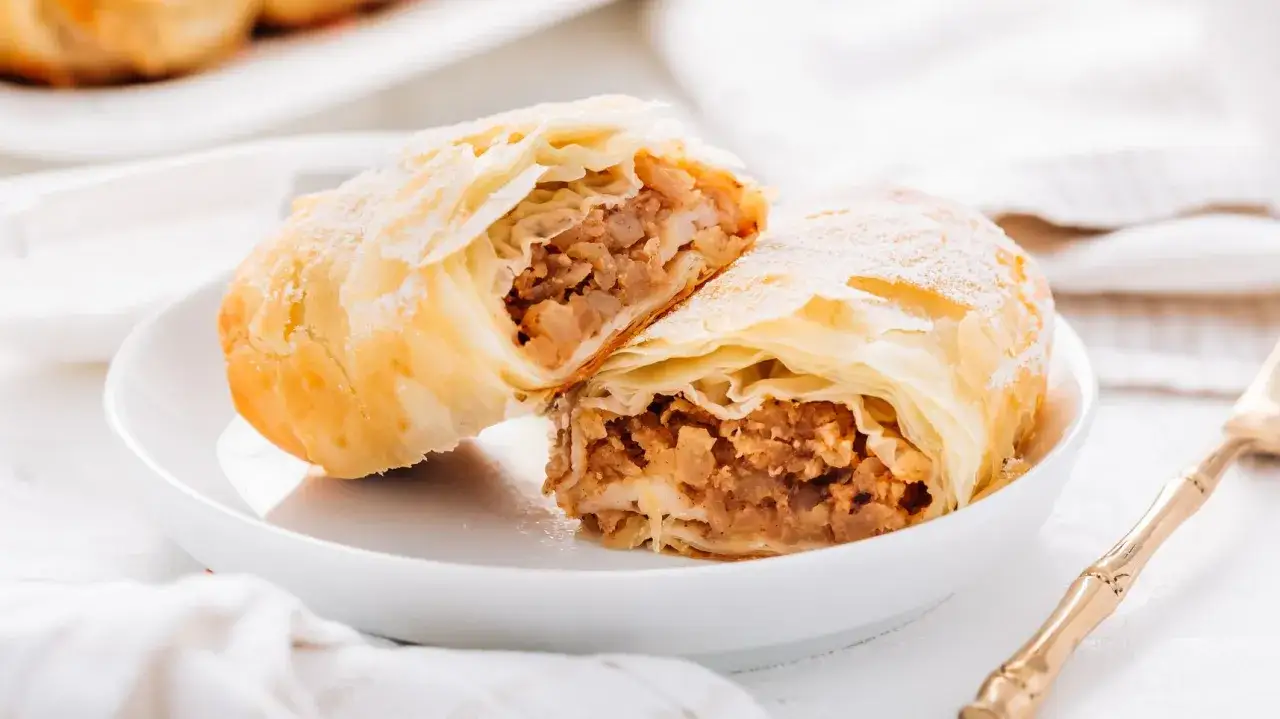 Delizioso strudel di mele con pasta sfoglia, tagliato a metà per mostrare il ripieno succoso. Spolverato di zucchero a velo, è pronto per essere gustato.