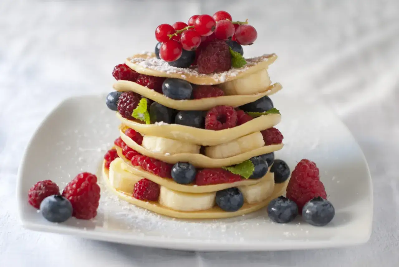 Torre di pancake senza zucchero con frutti di bosco freschi e banane, spolverata di zucchero a velo.