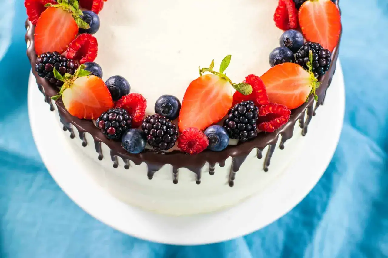 Delizioso drip cake bianco con fragole, lamponi, mirtilli e more, decorato con cioccolato fuso che cola.