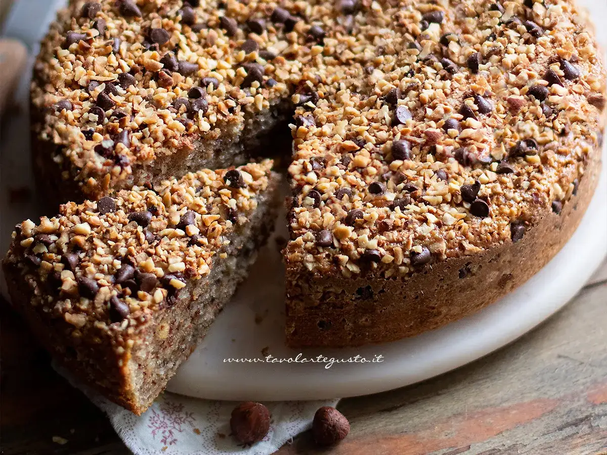 Deliziosa torta di nocciole con gocce di cioccolato e granella croccante, una fetta &egrave; gi&agrave; stata servita.