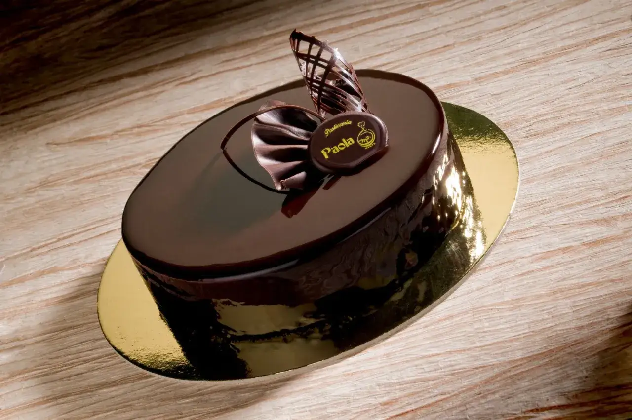 Elegante torta compleanno uomo con panna, glassata al cioccolato e decorata con riccioli di cioccolato e un medaglione.