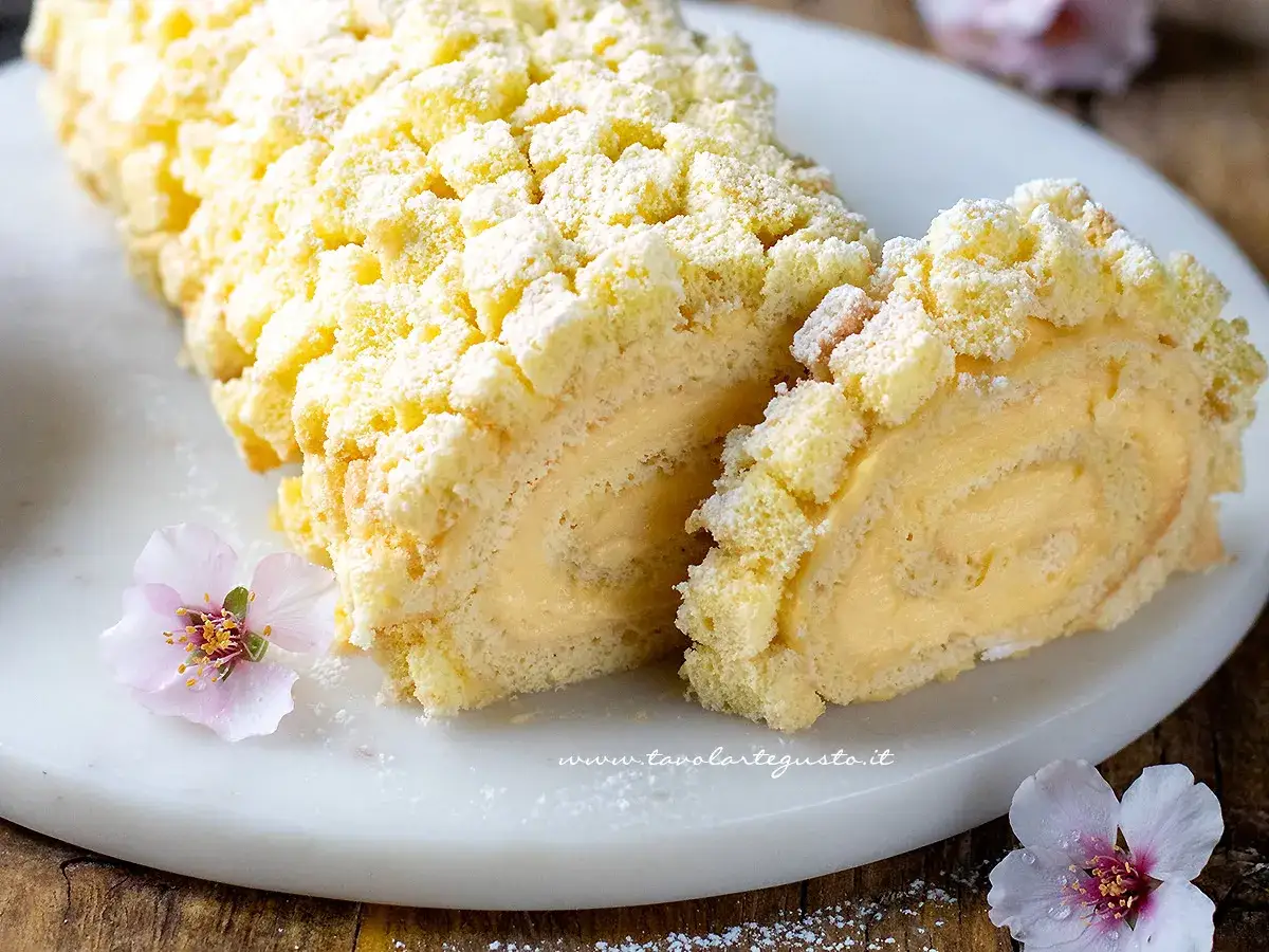 Rotolo di pasta biscotto ripieno di crema, cosparso di zucchero a velo e decorato con fiori rosa.