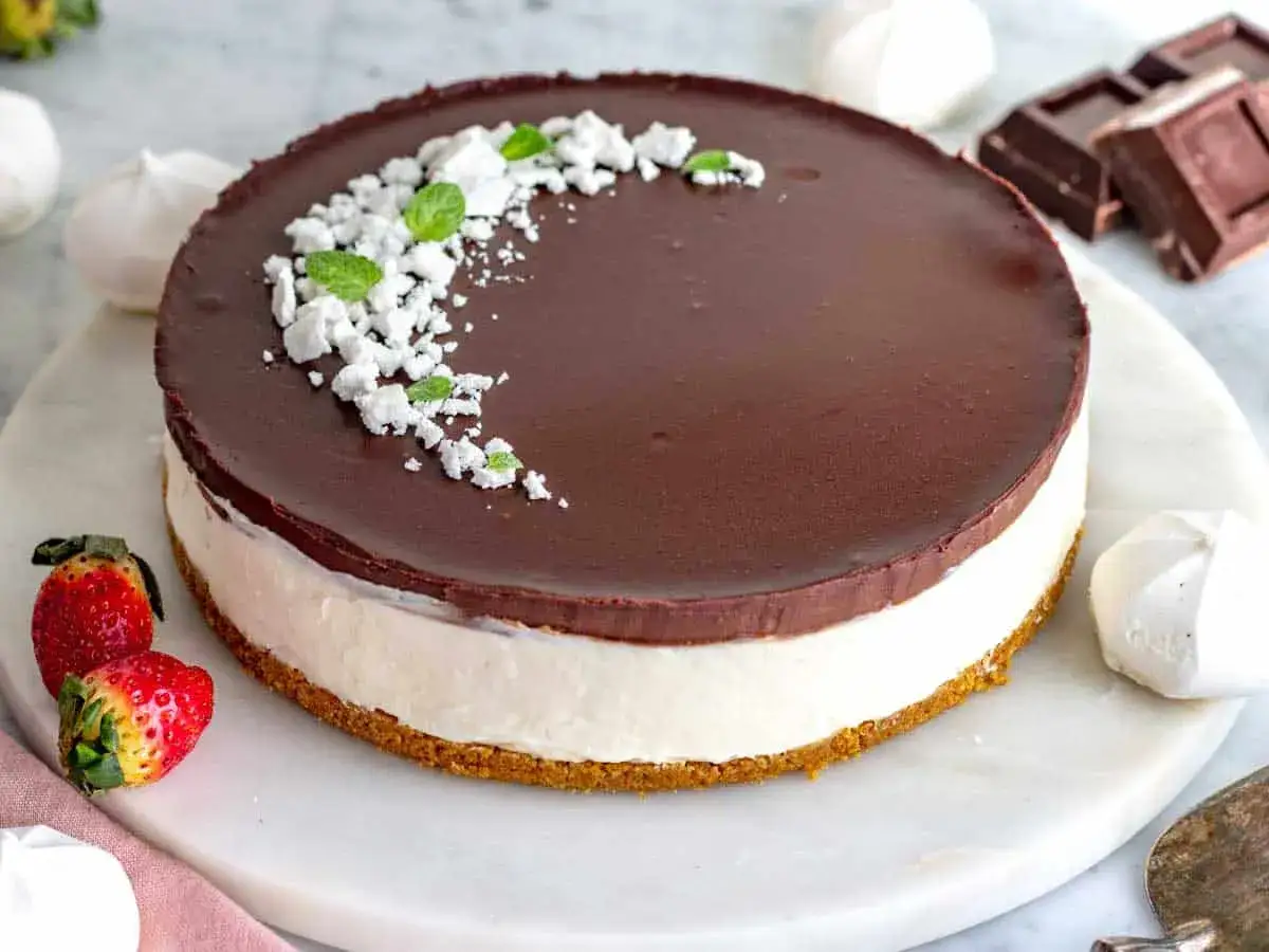 Torta con base croccante, ripieno bianco e lucida ganache cioccolato per copertura, decorata con meringa sbriciolata e menta.