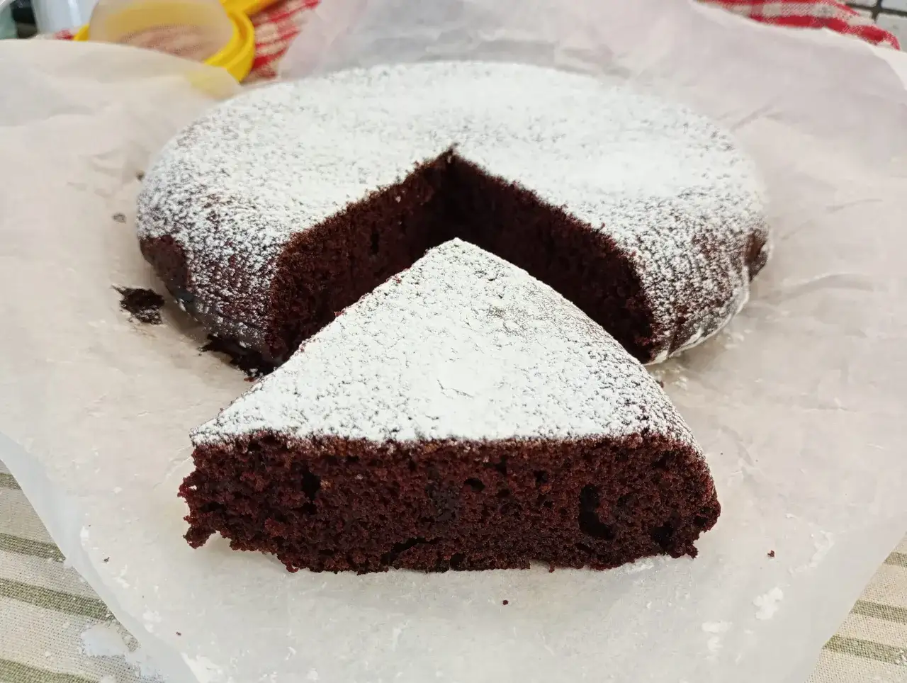 Una deliziosa torta all'acqua al cacao, soffice e spolverata di zucchero a velo, con una fetta tagliata.