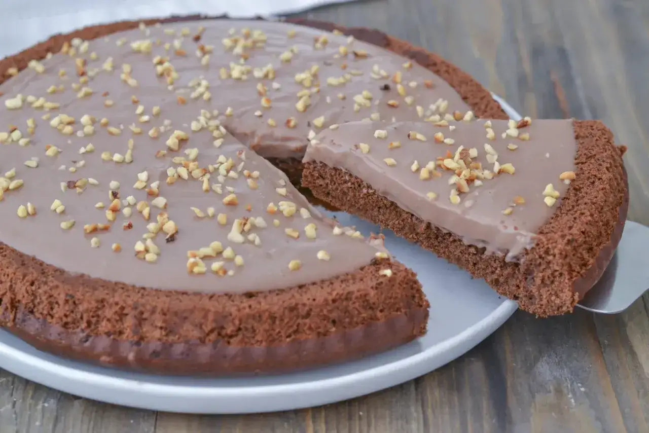 Una deliziosa torta cioccolato e nocciole, con una fetta appena tagliata, guarnita con granella croccante.