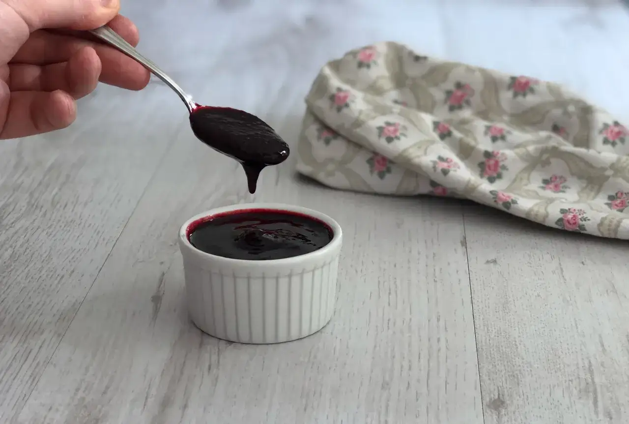 Un cucchiaio raccoglie un denso coulis frutti di bosco, pronto per guarnire un dessert.