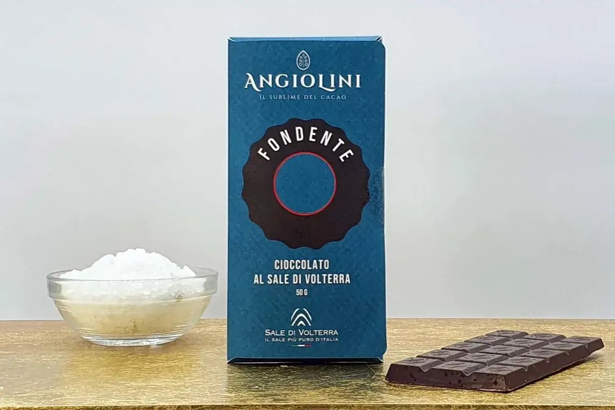Scatola di cioccolato fondente Angiolini con sale di Volterra, accanto a una ciotola di sale grosso e una tavoletta di cioccolato.